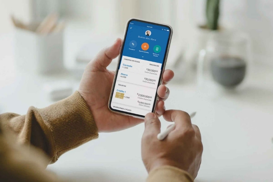 Persona usando un teléfono móvil con una app bancaria abierta mostrando saldos y tarjetas.