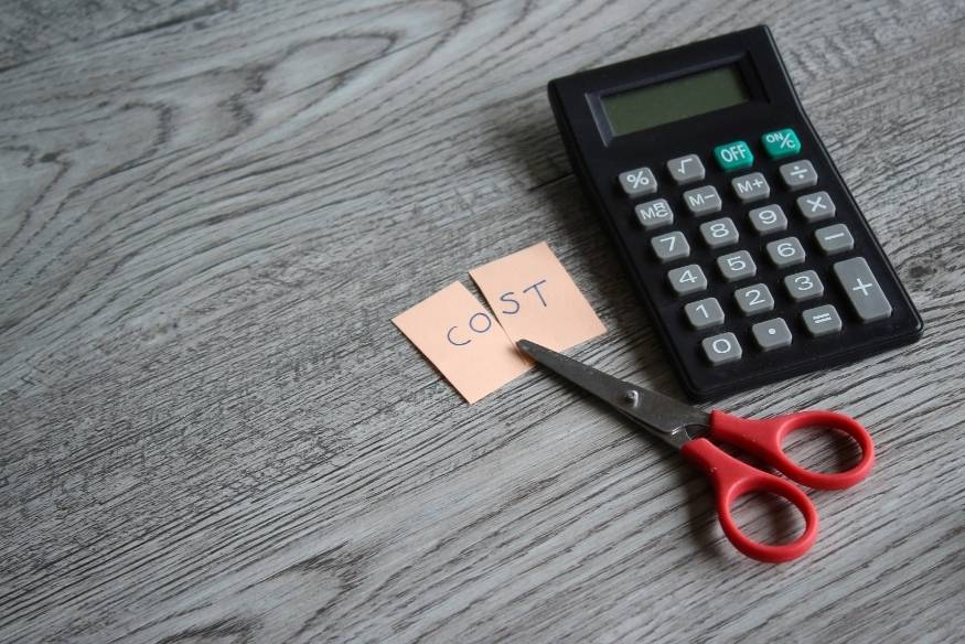 Calculadora junto a unas tijeras cortando papel con la palabra "cost".