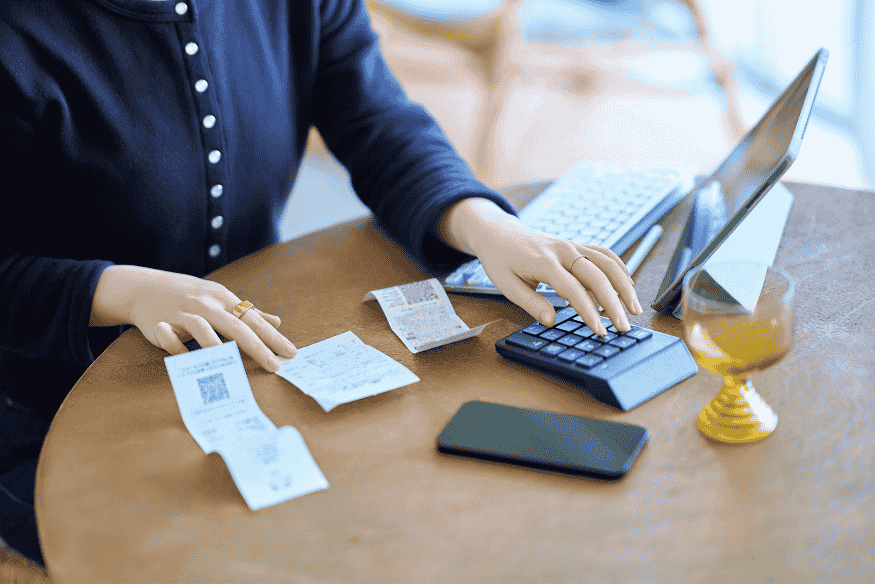 Persona revisando gastos diarios con calculadora, recibos y portátil para controlar gastos hormiga