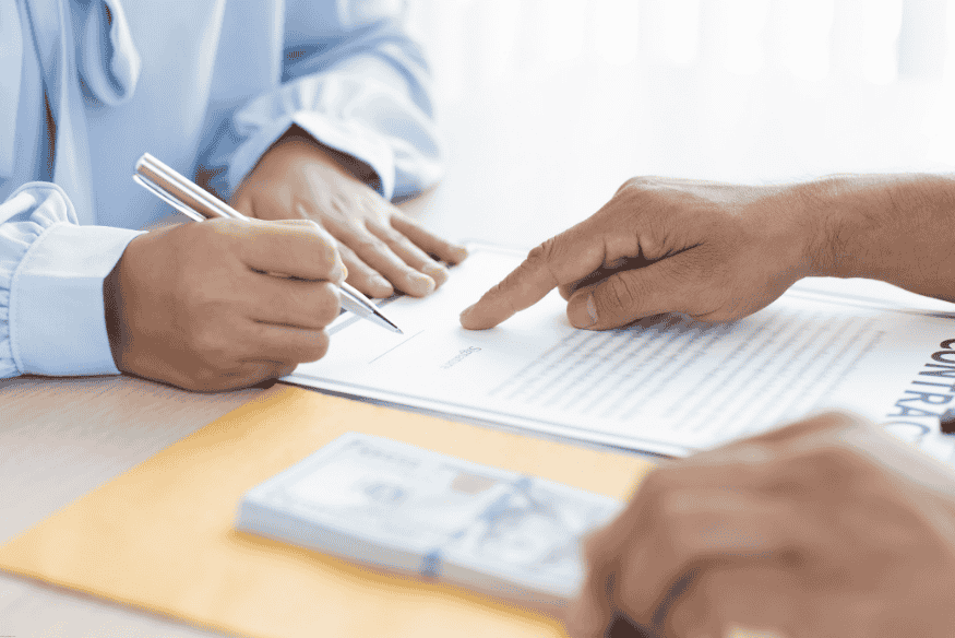 Persona firmando un contrato financiero con fajos de billetes sobre la mesa.