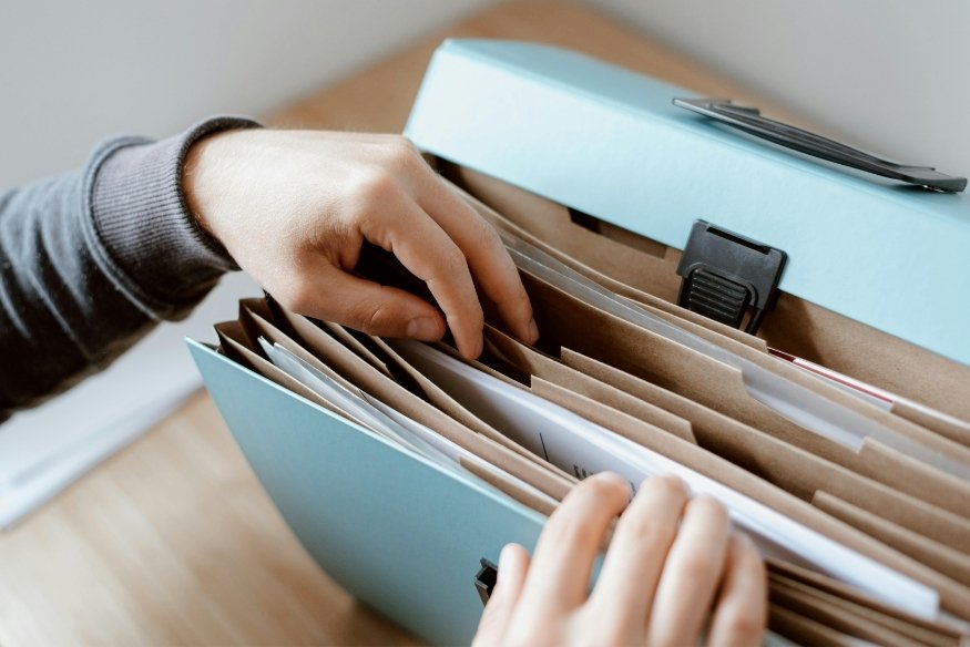 Mano revisando archivos y documentos organizados en un archivador.