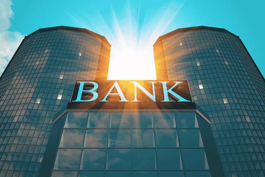 Fachada moderna de un banco con luz solar entre dos torres.