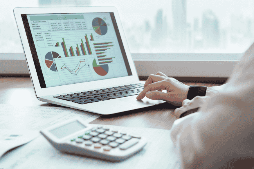 Laptop mostrando gráficos financieros y estadísticas con una calculadora al lado.