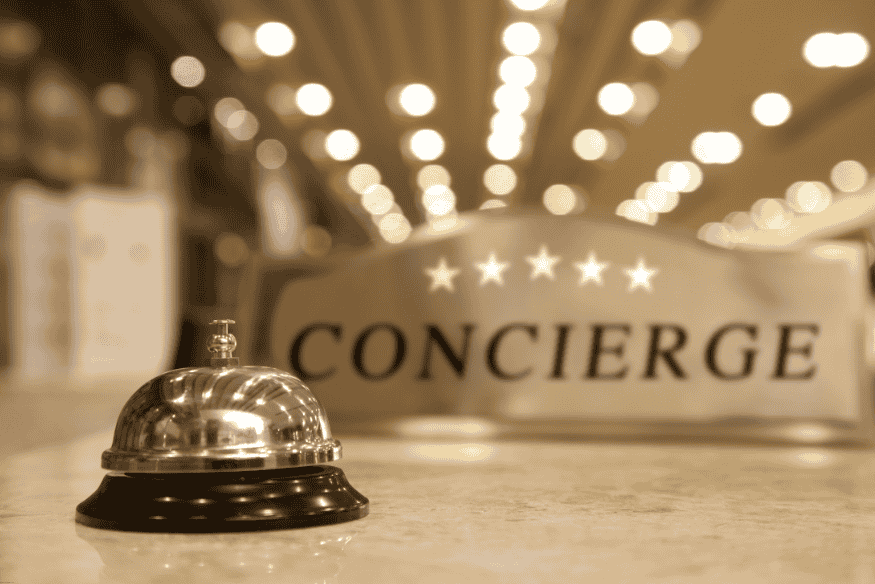 Campanilla de hotel frente a cartel de concierge con estrellas, simbolizando atención exclusiva.