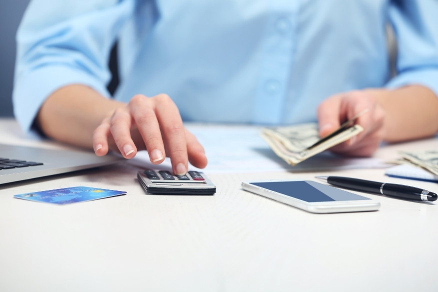 Manos usando calculadora con billetes y tarjeta de crédito sobre la mesa.