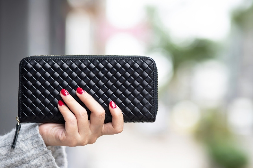 Mano con uñas pintadas de rojo sosteniendo una cartera negra tejida.