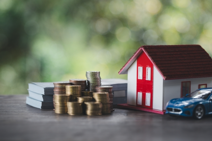 Modelo de casa, carro e pilhas de monedas representando compras grandes con tarjeta de crédito