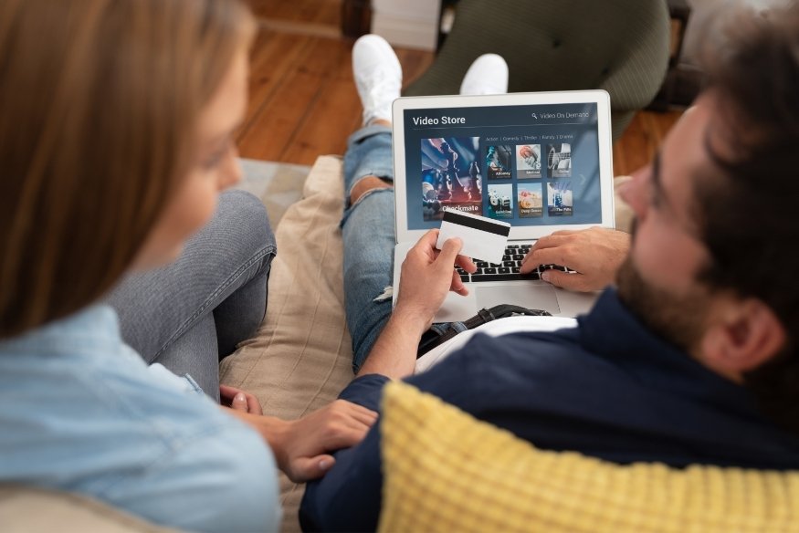 Pareja sentada en el sofá usando laptop y tarjeta de crédito para compras en línea.