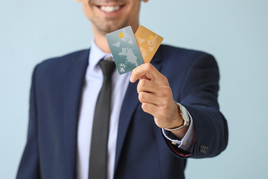 Hombre con traje sosteniendo dos tarjetas de crédito, sonriendo.