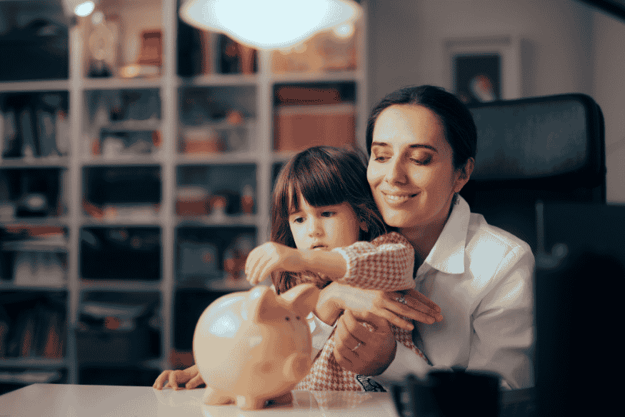 Madre enseñando a su hija pequeña a ahorrar usando una alcancía.