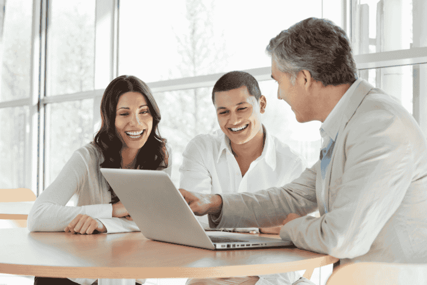 Pareja joven sonriendo mientras consulta en una laptop con un asesor financiero.
