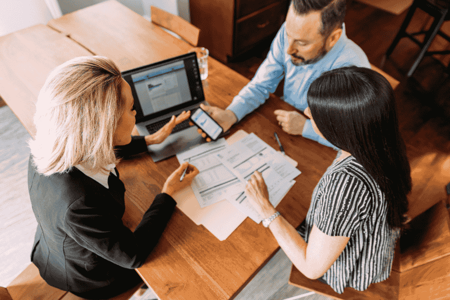 Asesora financiera mostrando documentos a una pareja en una mesa de trabajo.