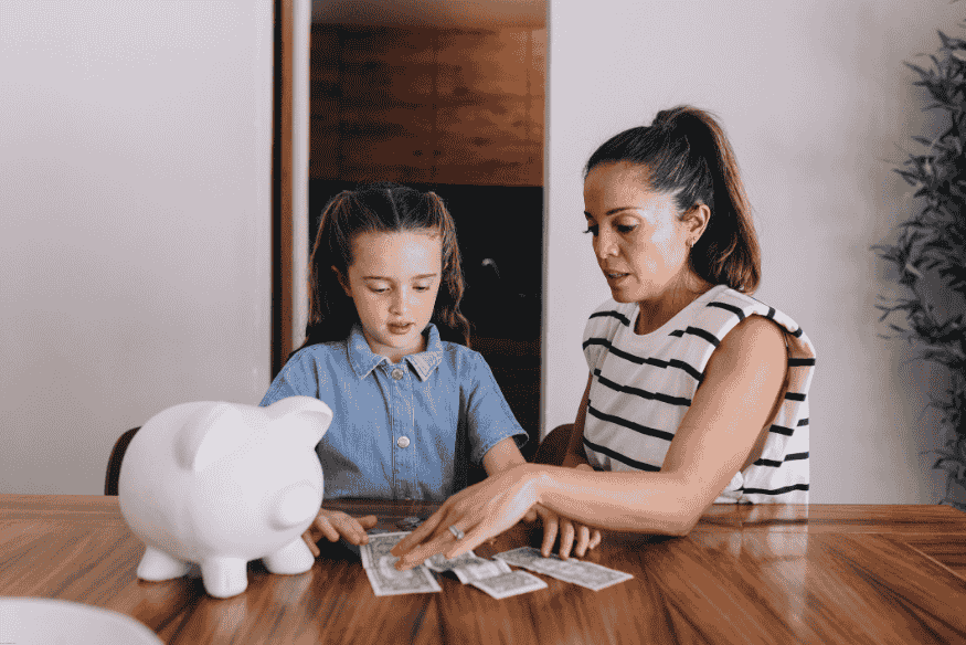 Madre e hija revisando billetes sobre la mesa con una alcancía al lado.