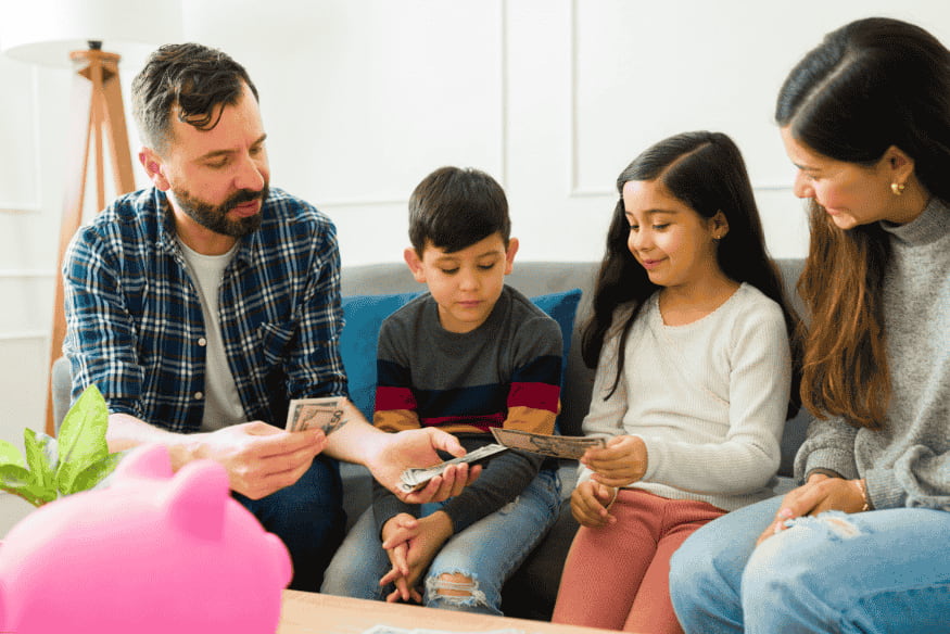 Familia sentada en el sofá enseñando a sus hijos a contar y manejar dinero.