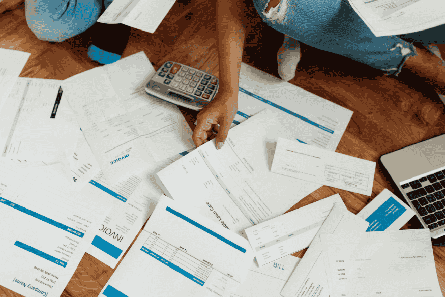 Persona revisando muchas facturas en el suelo mientras usa una calculadora.