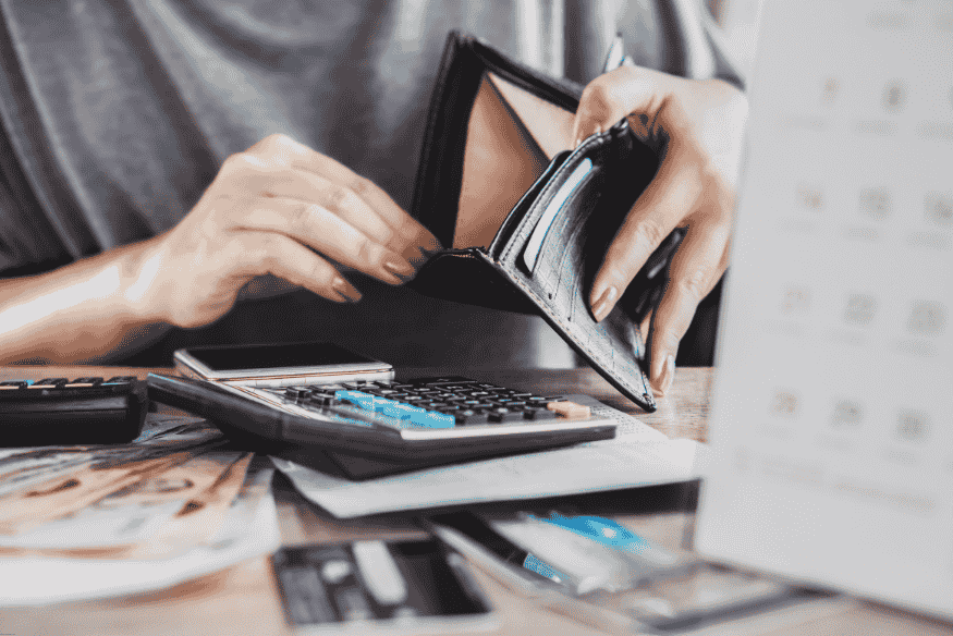 Persona revisando una billetera vacía junto a una calculadora y facturas.