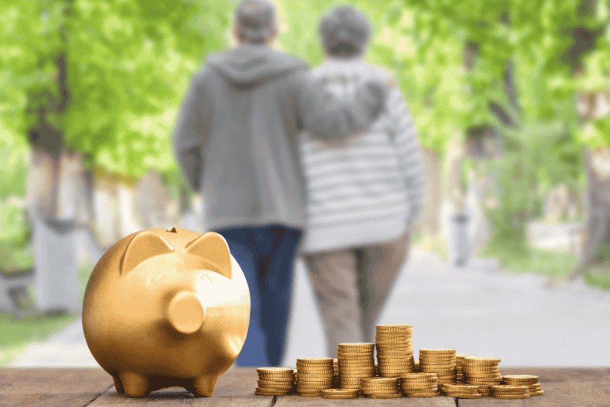 Pareja de adultos mayores caminando abrazados con una alcancía dorada y monedas al frente.