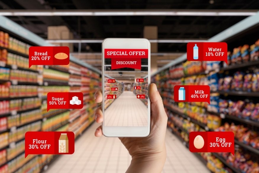 Mano sosteniendo teléfono móvil en un pasillo de supermercado con etiquetas digitales de descuentos.