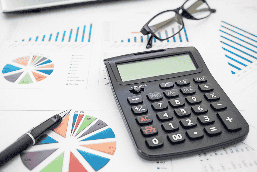 Calculadora, gráficos de pastel y de barras, bolígrafo y gafas sobre informes financieros.