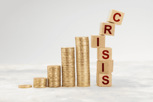 Torres de monedas en crecimiento junto a bloques que forman la palabra "crisis", inclinándose.