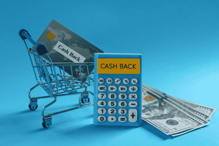 Carrito de compras con tarjeta de crédito y calculadora con la palabra "cash back", junto a billetes de dólar.