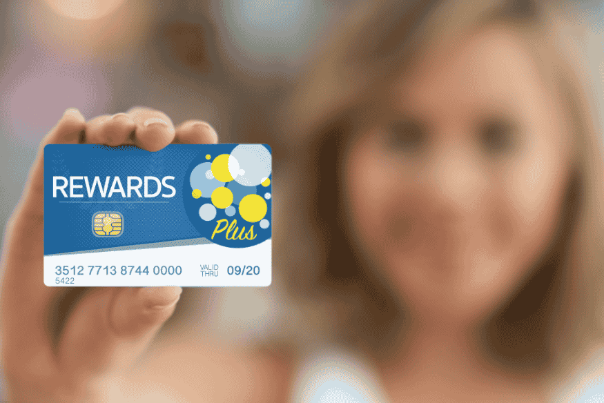 Mujer mostrando tarjeta de recompensas "Rewards Plus" enfocada en la cámara.