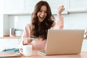 Mujer emocionada usando una tarjeta de crédito frente a una laptop.