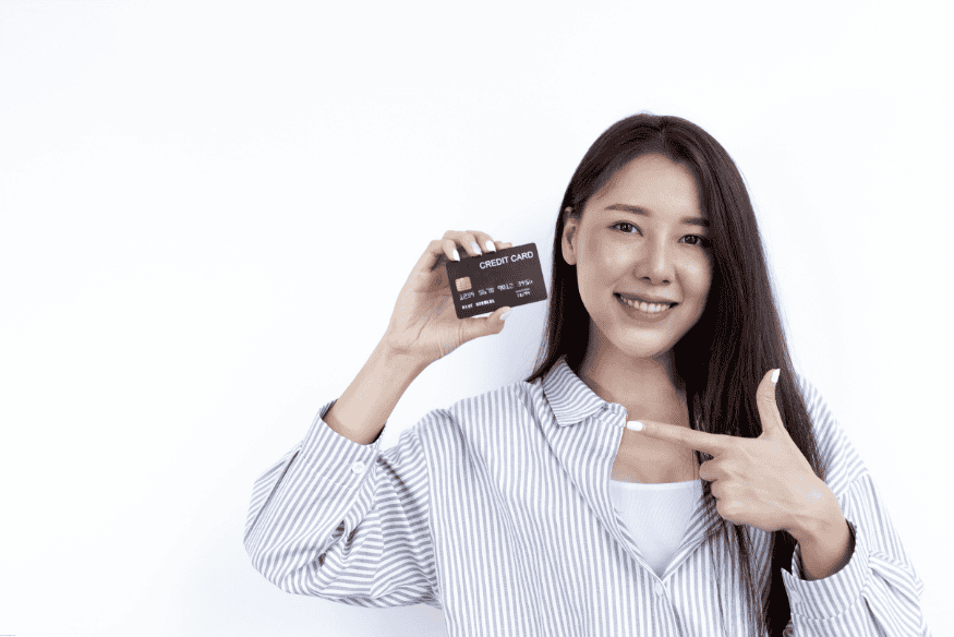 Mujer joven sonriente señalando una tarjeta de crédito negra.