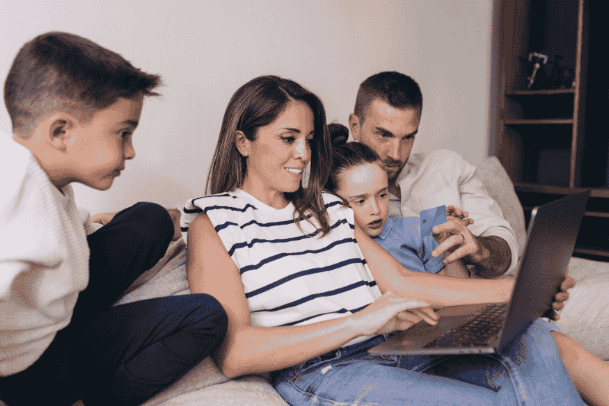 Familia reunida en el sofá usando una laptop y una tarjeta de crédito.