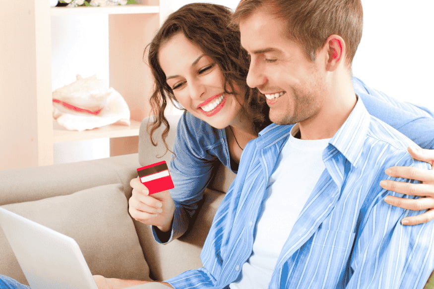Pareja feliz usando una tarjeta de crédito mientras navegan en una laptop.