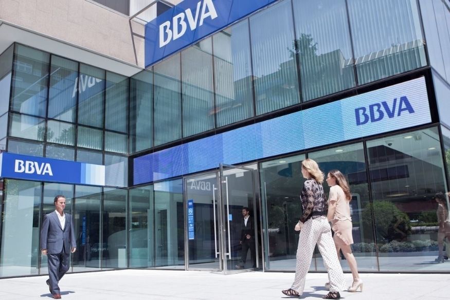 Fachada de una sucursal del banco BBVA con personas entrando.