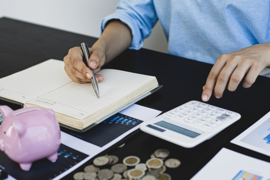 Persona revisando su presupuesto con una libreta, calculadora y monedas sobre la mesa.