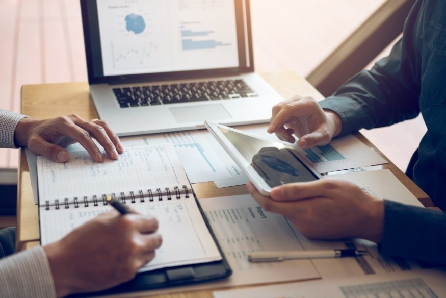 personas analizando gráficos financieros con tablet, ordenador y libreta