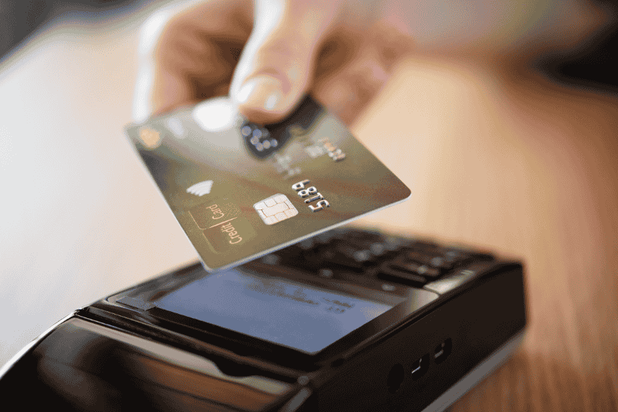 Persona utilizando una tarjeta de crédito con tecnología contactless en un lector de pagos.