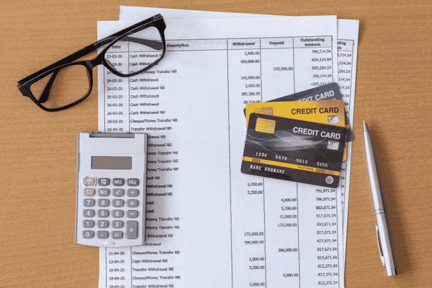 Tarjetas de crédito, calculadora, gafas y estados de cuenta sobre una mesa, reflejando planificación financiera.
