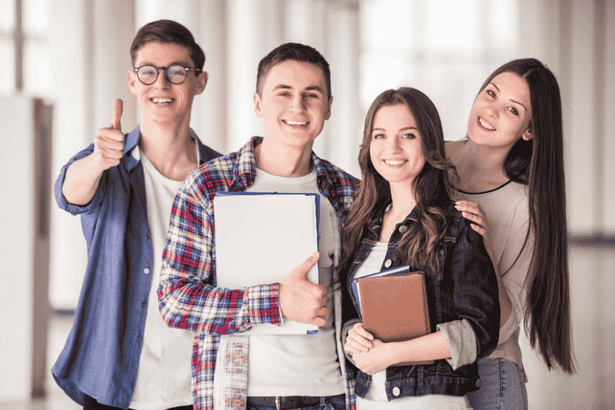 Grupo de estudiantes sonrientes con carpetas y mochilas en un pasillo universitario.