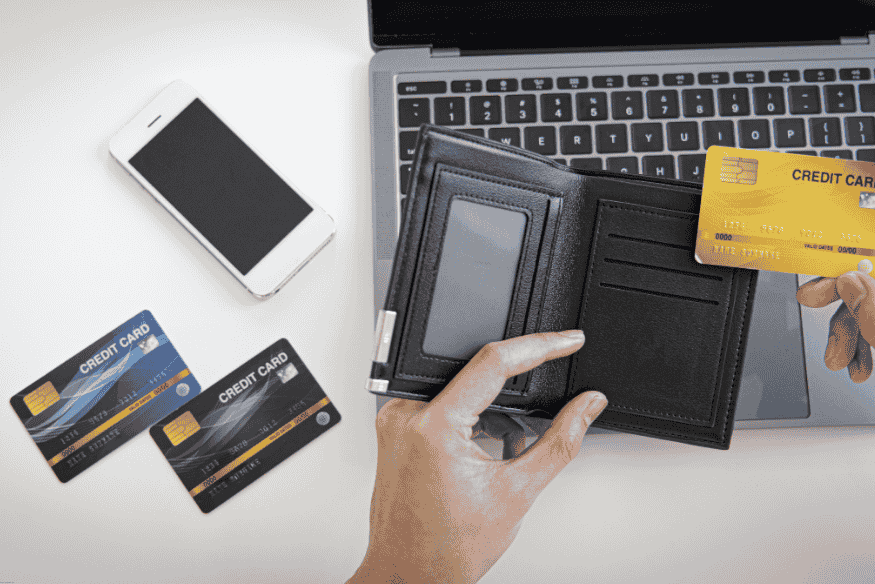 Mano sacando tarjeta de crédito dorada frente a laptop