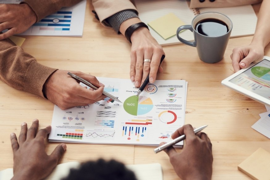 Grupo de personas analizando gráficos y datos financieros en una reunión.